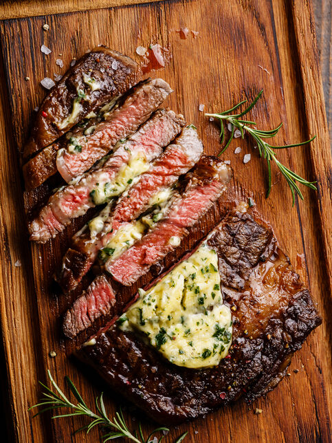 Sliced grilled Medium rare barbecue steak Ribeye with herb butter on cutting board close up